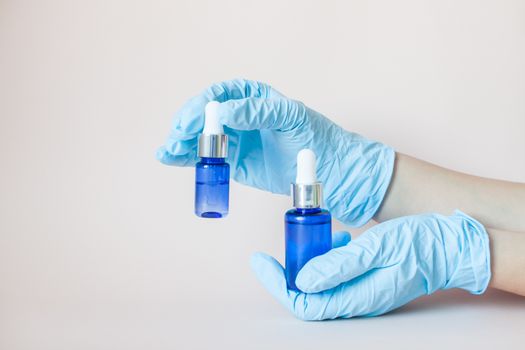 Bottles with serum for the face in his hands in protective medical rubber gloves on a light background. Beauty industry.