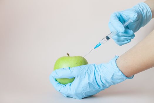 Green apple in hands with a syringe in protective medical rubber gloves on a light background.
