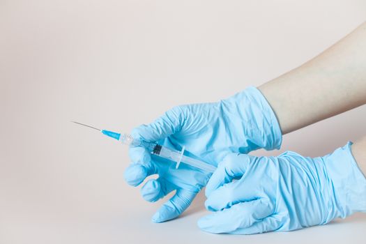 Syringe in hands in protective medical rubber gloves on a light background.
