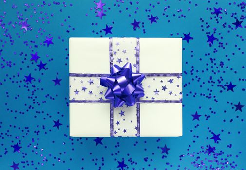 Gift box and stars on blue background. Monochrome flat lay.