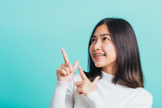 Portrait of Asian teen beautiful young woman smile have dental braces on teeth laughing point finger side away blank copy space, studio shot isolated on blue background, medicine and dentistry concept