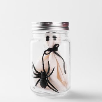 Funny Halloween day decoration party, The white ghost scary face and black spider in jar glass, studio shot isolated on white background, Happy holiday concept