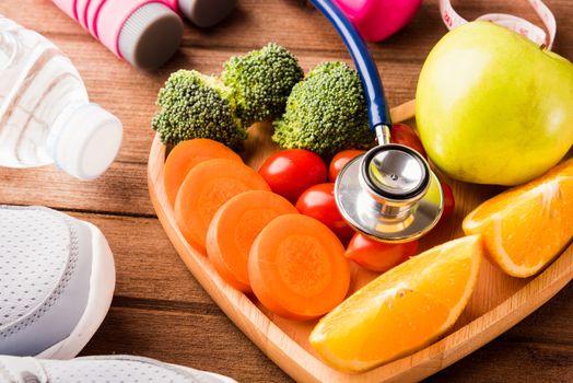 Top view of fresh fruits and vegetables in heart plate wood (apple, carrot, tomato, orange, broccoli) and sports equipment and doctor stethoscope on wooden table, Healthy lifestyle diet food concept