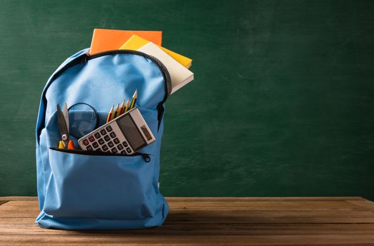 Front of stylish school bag backpack supplies and stationery accessory on a table desk at the green chalkboard, Back to school education concept