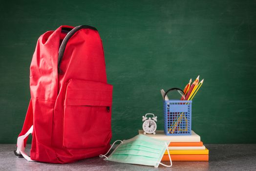 Front school backpack and accessories with face mask protect on table at chalkboard, student bag supplies at classroom backboard, Back to school education new normal outbreak COVID-19 or coronavirus