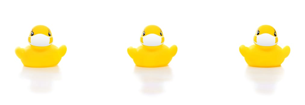 cute yellow rubber ducks in face masks on white background, concept of social distancing flu prevention, people should practice social distancing during situation of COVID-19 to stop the pandemic