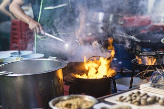 Street food in Bangkok Bangkok Thailand - Oct 24, 2020 :- Chef cooking with fire with frying pan on gas hob at yoawarat Bangkok Thailand.