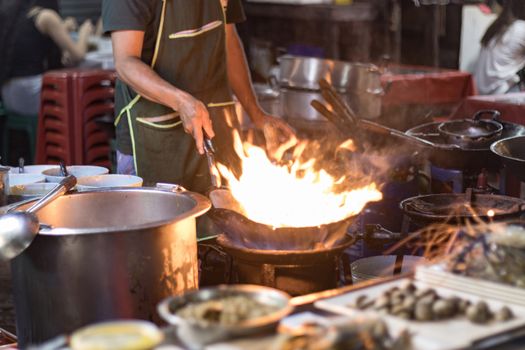 Street food in Bangkok Bangkok Thailand - Oct 24, 2020 :- Chef cooking with fire with frying pan on gas hob at yoawarat Bangkok Thailand.