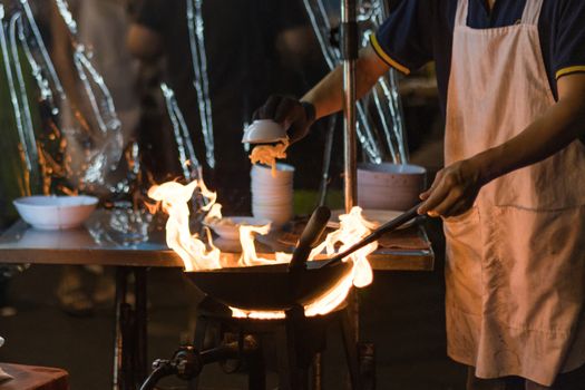 Street food in Bangkok Bangkok Thailand - Oct 24, 2020 :- Chef cooking with fire with frying pan on gas hob at yoawarat Bangkok Thailand.