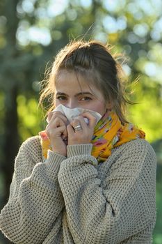 Girl in fall autumn park sneezing in tissue