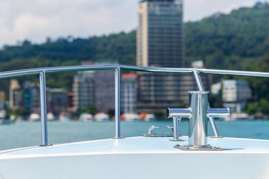 boat bow with stainless steel anchor system on background of turquoise sea or lake and green mountain city on sunny day, boatman set the bow on the right direction to the pier.