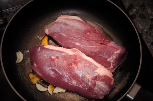 A tasty uncooked goose's magret (filet) with orange and garlic in a cooking pan