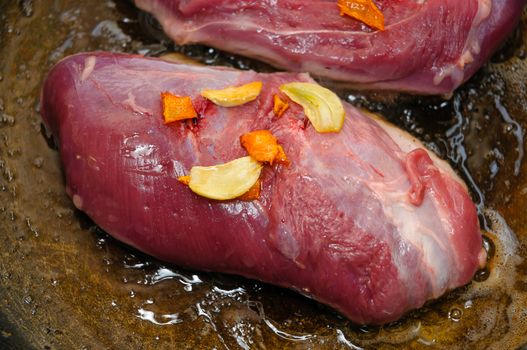 A tasty uncooked goose's magret (filet) with orange and garlic in a cooking pan