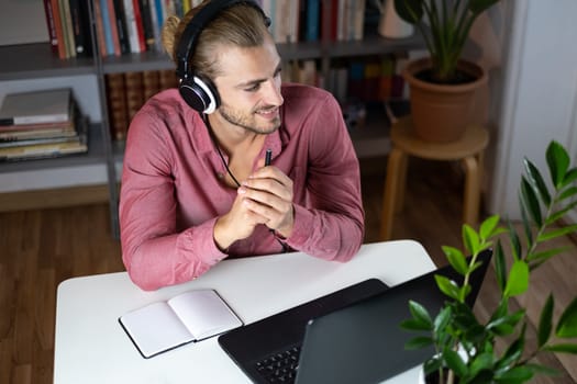 Handsome young caucasian man using computer working at home and talking with headphones feeling happy with smile showing teeth