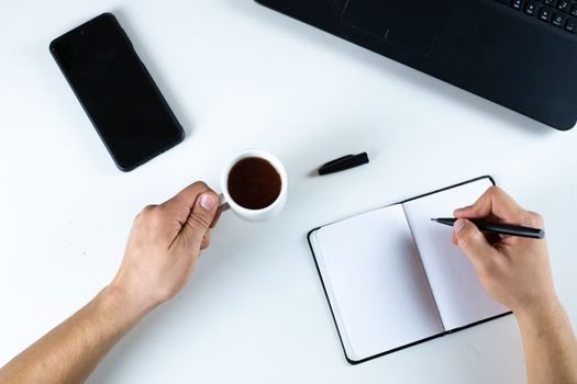 White table with computer, hands, mobile, pen, tea and notebook from above. Concept ready to work