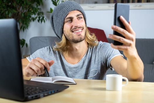 Handsome young caucasian man using computer working at home and talking with mobile feeling happy with smile showing teeth
