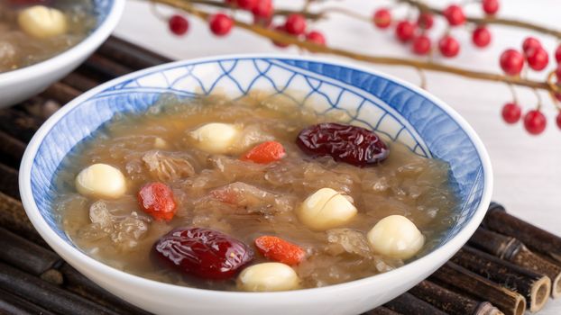 Close up of traditional Chinese sweet snow white fungus soup with lotus seed, red dates (jujube) and wolfberry (goji berry, gojiberry) on white background.