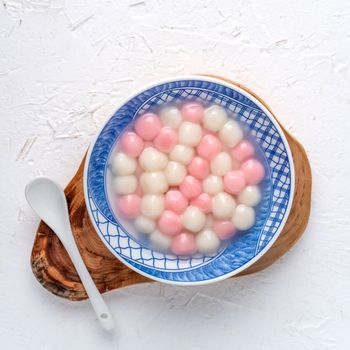 Top view of red and white tangyuan (tang yuan, glutinous rice dumpling balls) in blue bowl on white background for Winter solstice festival food.