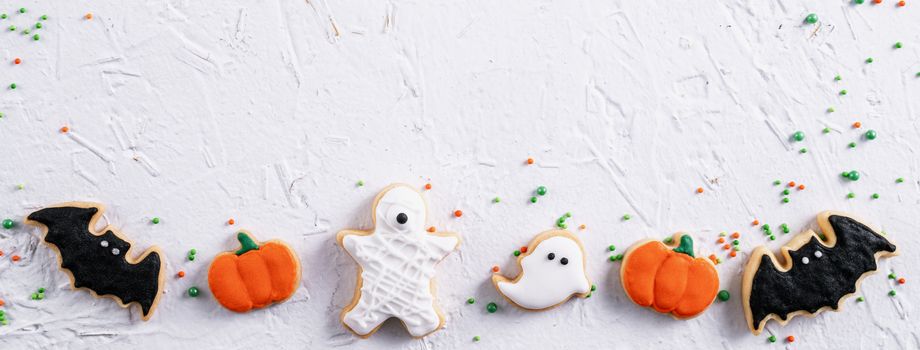 Top view of Halloween festive decorated icing gingerbread sugar cookies on white background with copy space and flat lay layout.