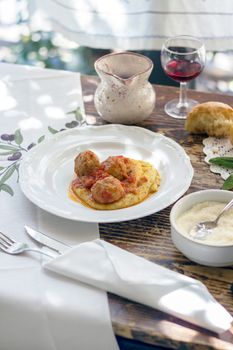 Polenta with meatballs in tomato sauce. Traditional italian pork and beef meatballs served on polenta with tomato sauce, basil, parmesan and a drizzle of olive oil. In the woodden table a glass of red wine and parmisan.