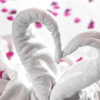 Two towel swans on the bed, sprinkled with pink petals. The towel look like heart shape and it's prepare for couple in honey moon. Ideal for events and concepts.