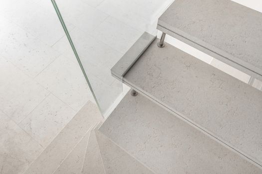 Grey microcement stairs with glass handrail. Stairs viewed from above. Modern design and innovative material. Glass railing.
