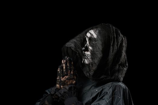 woman with a make-up skeleton stands in black clothes and a transparent hood, hands are folded in a prayer pose, black background