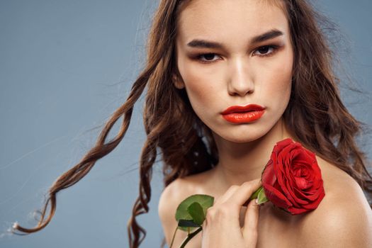 Woman portrait with red rose near the face on gray background and makeup curly hair. High quality photo