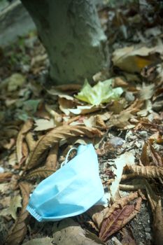 Used surgical mask lying on dry leaves in the field. Pollution in nature