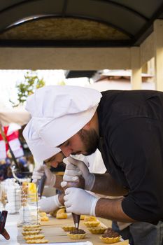 TBILISI, GEORGIA - OCTOBER 08, 2017: Confectioner chef cooking dessert scene, chef decorates cake and working in the street of Tbilisi on the city festival.