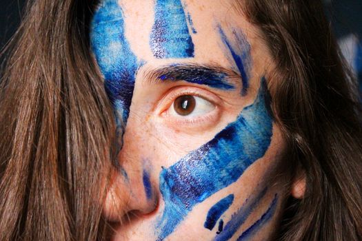 Painted face with acrylic blue and white colors. Young beautiful woman portrait, close-up photo.