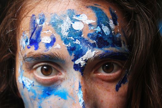 Painted face with acrylic blue and white colors. Young beautiful woman portrait, close-up photo.