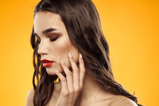 Beautiful brunette naked shoulders bright makeup red lips hairstyle close-up yellow background. High quality photo