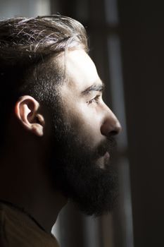 Handsome serious man portrait on the dark background, sunlight and room.