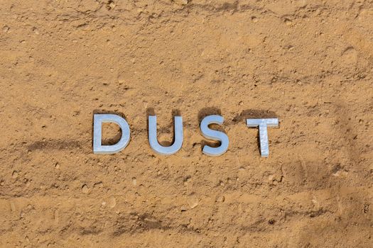 the word dust laid with silver metal letters on dusty road surface - close-up flat lay perspective under direct sunlight