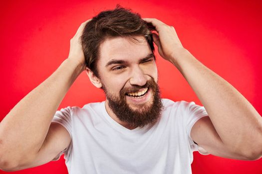 A man in a white T-shirt with a beard gestures with his hands emotions red background. High quality photo