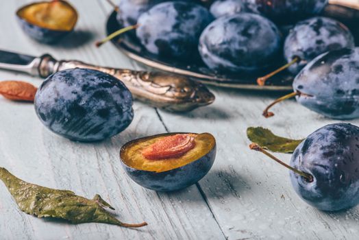 Ripe plums with sliced fruits, leaves and vintage knife over light wooden surface