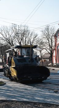 ndustrial asphalt paver machine laying fresh asphalt on road construction site on the street. A Paver finisher placing a layer of a new hot asphalt on the roadway on a construction site. Repairing