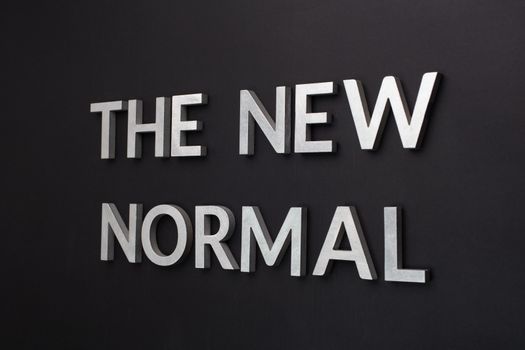 words the new normal laid with silver metal letters on flat black matte surface in tilted perspective with dark lightiing