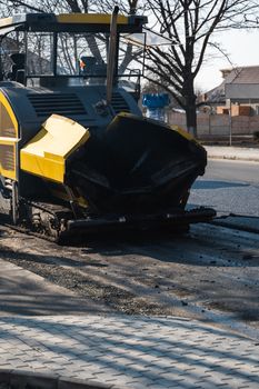 ndustrial asphalt paver machine laying fresh asphalt on road construction site on the street. A Paver finisher placing a layer of a new hot asphalt on the roadway on a construction site. Repairing