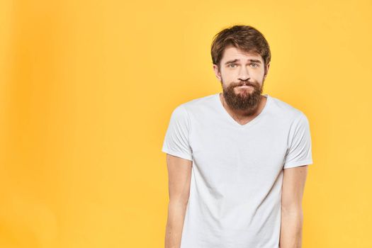 Bearded man in a white T-shirt gestures with his hands emotions studio yellow background. High quality photo