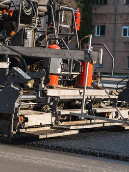 ndustrial asphalt paver machine laying fresh asphalt on road construction site on the street. A Paver finisher placing a layer of a new hot asphalt on the roadway on a construction site. Repairing