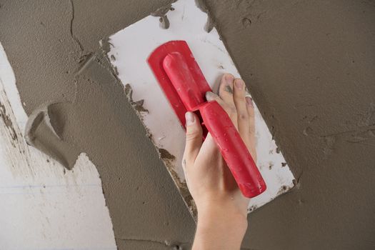 A worker plasters the wall with a spatula and applies a cement mix solution. The repairman lays the plaster on the drywall. Handyman repairs home. Laborer restore dwelling. Specialist covers up cracks