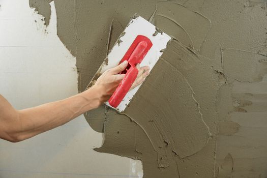 A worker plasters the wall with a spatula and applies a cement mix solution. The repairman lays the plaster on the drywall. Handyman repairs home. Laborer restore dwelling. Specialist covers up cracks