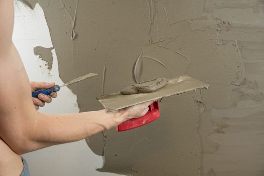 A worker plasters the wall with a spatula and applies a cement mix solution. The repairman lays the plaster on the drywall. Handyman repairs home. Laborer restore dwelling. Specialist covers up cracks