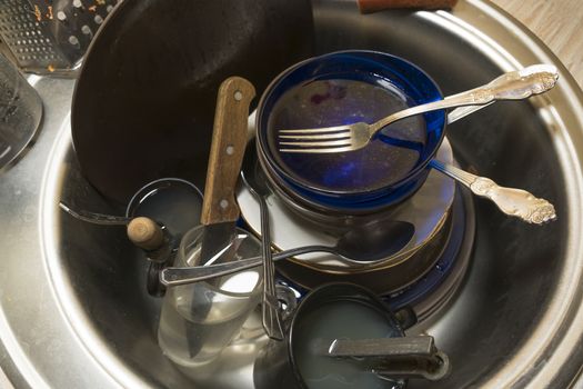 A pile of unwashed dirty dishes in the sink in the kitchen or dining room.Work at home for a housewife. There are dirty plates, mugs, cups, spoons, forks and a knife in the sink.Washing dirty dishes.