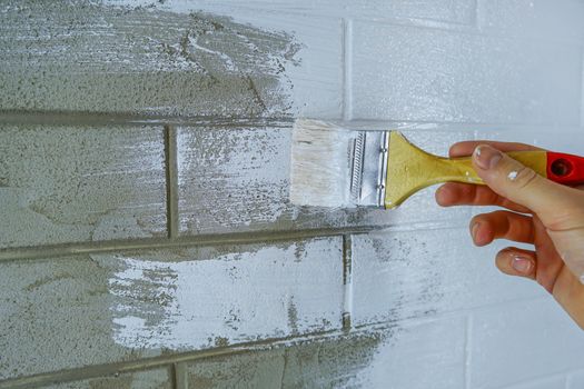 A construction worker applies paint to a brick wall.The painter paints primers the walls with a brush, makes repairs in the house or room.Reconstruction of the building, specialist restores the wall           