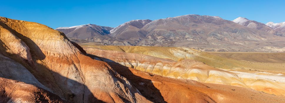 Panoramic shot of massive red mountains in Kyzyl-Chin valley, also called Mars valley. Blue sky as a background. Altai, Siberia, Russia.