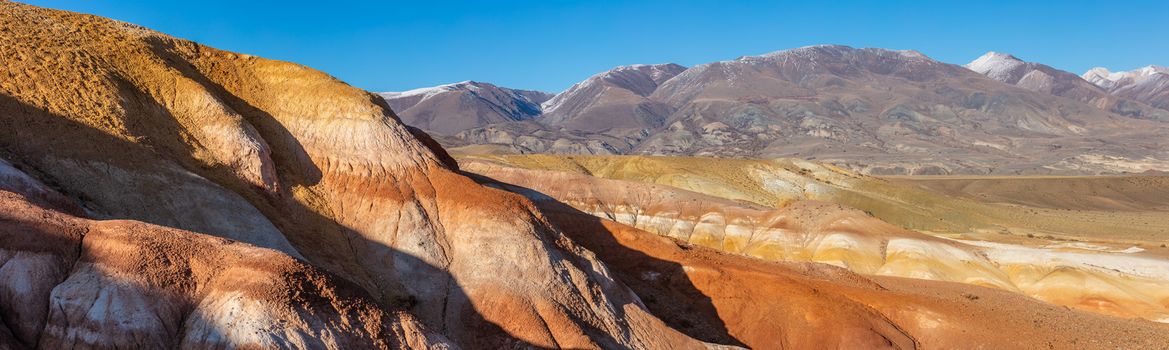 Panoramic shot of massive red mountains in Kyzyl-Chin valley, also called Mars valley. Blue sky as a background. Altai, Siberia, Russia.