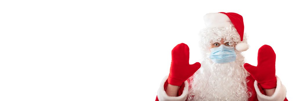 View of a man wearing Santa Claus costume, medical mask, having his both hands up, eyes wide open in warning gesture, isolated on white background. Banner size, copy space. Pandemic holiday concept.